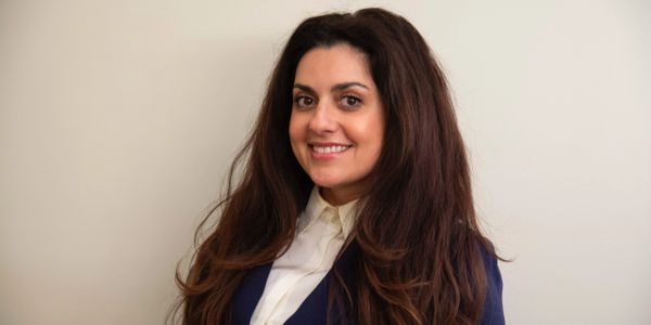 Smiling woman with long dark hair in professional attire against a plain background.