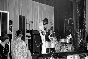 Black and white photo of a band performing on stage with audience watching.