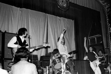 Black and white photo of a rock band performing on stage with energetic poses.