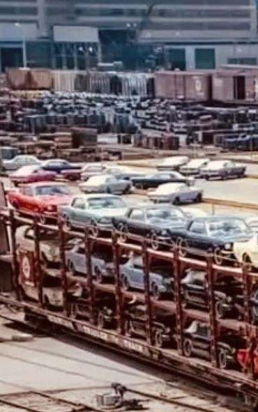 Vintage Ford factory with classic cars on transport train and parking lot.