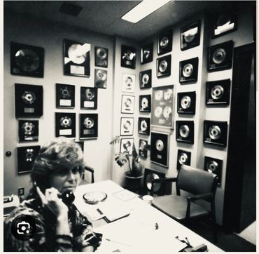 Woman on phone in office with many gold and platinum records on walls.