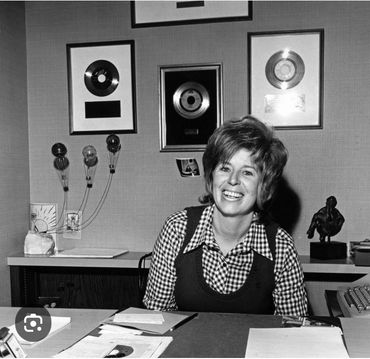 Smiling woman in an office with framed records on the wall.