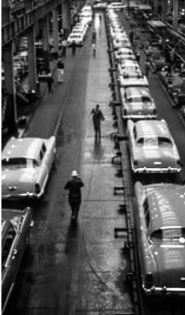 Vintage car assembly line inside a large factory with workers.