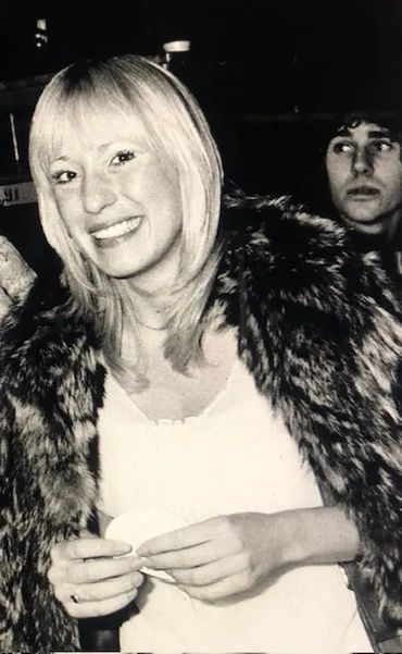 Smiling woman in a fur coat at a nighttime event.