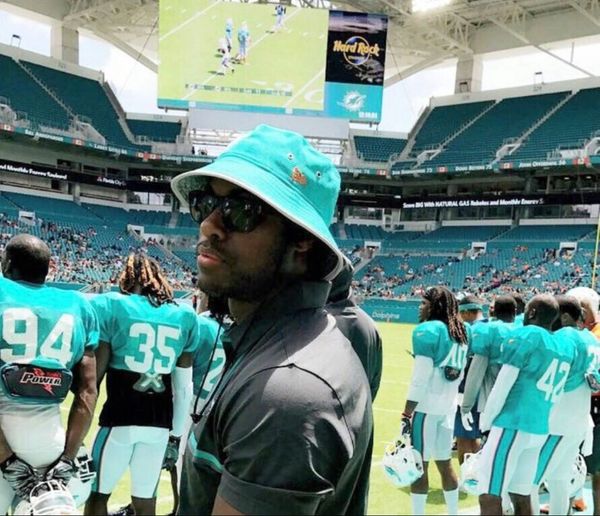 Dr. McKirven Ceus MD standing on football field with players in the background