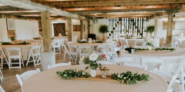 Rustic event space with decorated tables and white chairs.