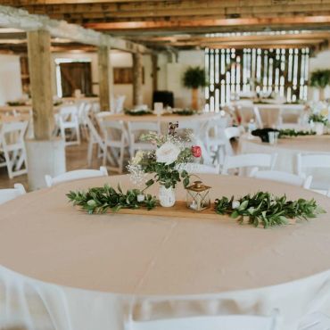 Rustic event space with decorated tables and white chairs.