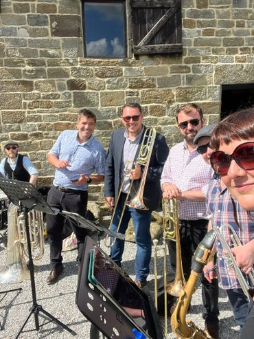 A group of musicians with brass instruments posing outdoors by a stone wall.