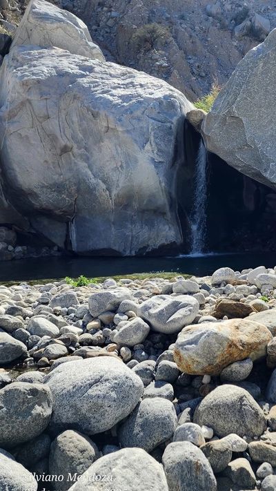A small waterfall flows between large rocks into a rocky stream.