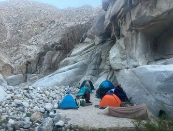 Several colorful tents set up in a rocky desert canyon area.