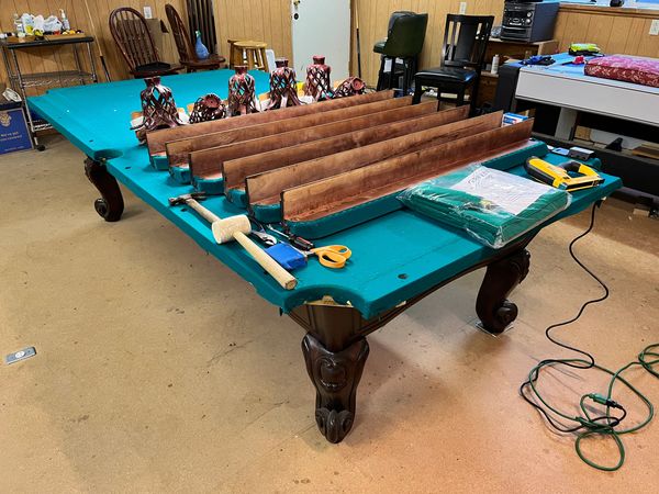 Disassembled pool table with tools and parts in a workshop.