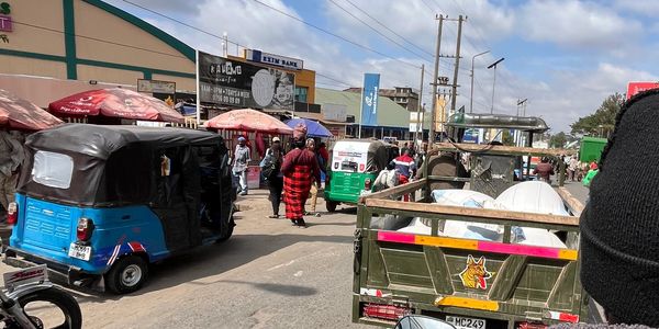 Busy street scene with tuk-tuks and pedestrians under a cloudy sky.