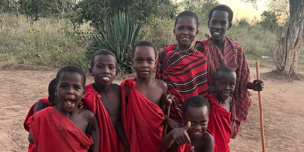 A group of children and a man in traditional red Maasai attire outdoors.