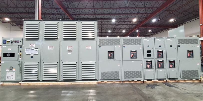 A wide row of custom-engineered gray electrical control cabinets in a warehouse