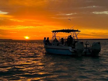 Boat with people silhouetted against a vibrant orange sunset over the water.