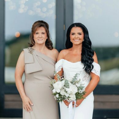 Bride and woman in elegant dresses smiling together.