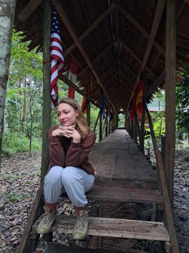 Mujer sentada en una estructura de madera rodeada de naturaleza.