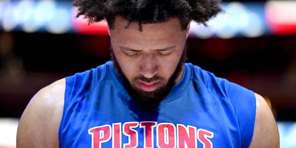 Basketball player in a Detroit Pistons jersey looking down thoughtfully.