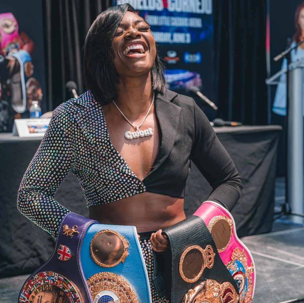A joyful female boxer holding multiple championship belts and wearing a sparkling outfit.