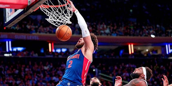 Basketball player in blue jersey dunking the ball during a game.