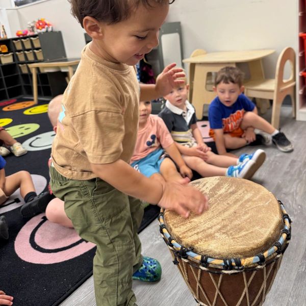 A young boy playing a drum in a classroom.
