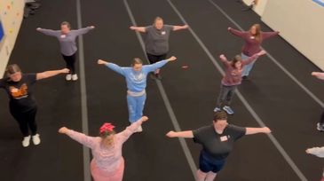 Group exercise class with participants stretching arms wide indoors.