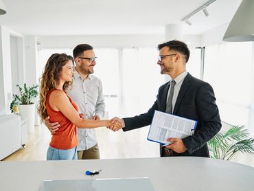 Happy couple shaking hands with a real estate agent in a bright home.