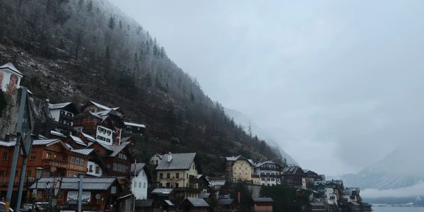 Snow-dusted houses on a foggy mountain slope by a lake.