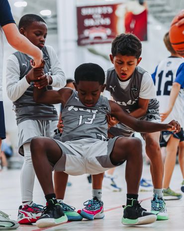Young basketball players helping a teammate up during a game.