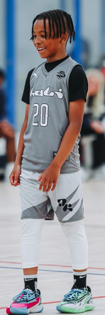 Young basketball player in gray uniform smiling on court.