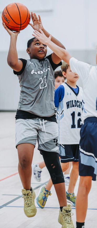 Young basketball player in gray jersey jumps for a shot during a game.