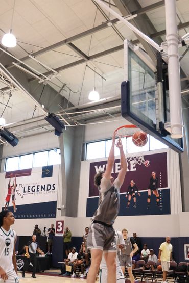 A basketball player in gray jumps to score a basket indoors.