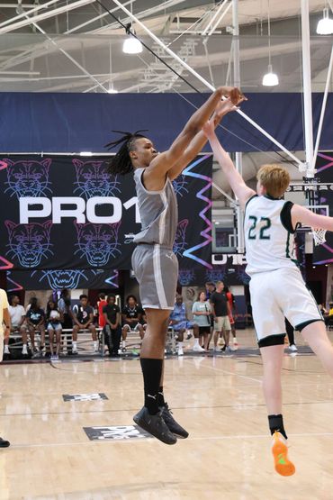 Two basketball players in mid-air during a jump shot attempt inside an indoor court.