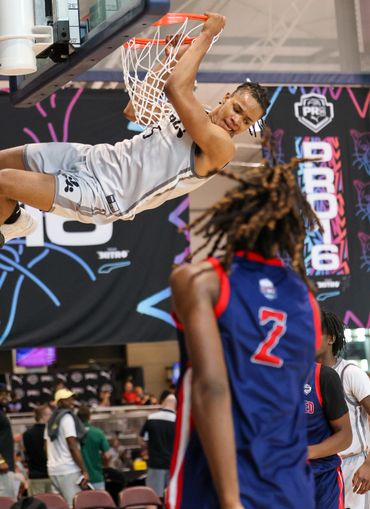 Basketball player in gray jersey dunks while opponent in blue watches.