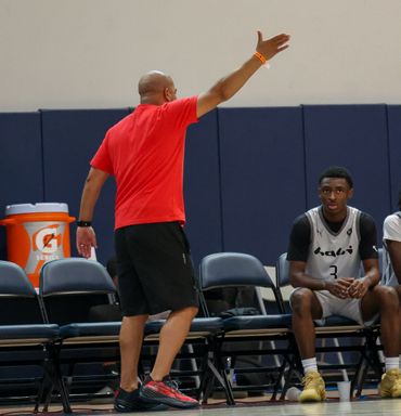 Coach in red directing basketball players seated on the bench.
