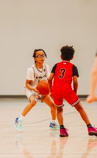 Two young boys playing basketball, one dribbling, the other defending.