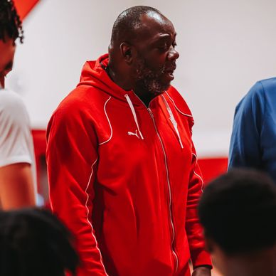 Man in a red Puma tracksuit speaking to a group indoors.