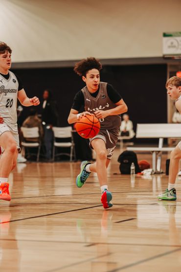 Teen basketball player dribbling past defenders in a gym game.