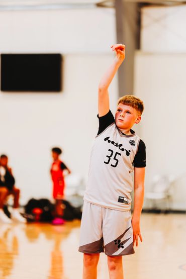 Young basketball player in white jersey practicing a shot on the court.