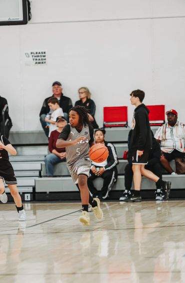 Young basketball player in gray jersey dribbling the ball on court during a game.