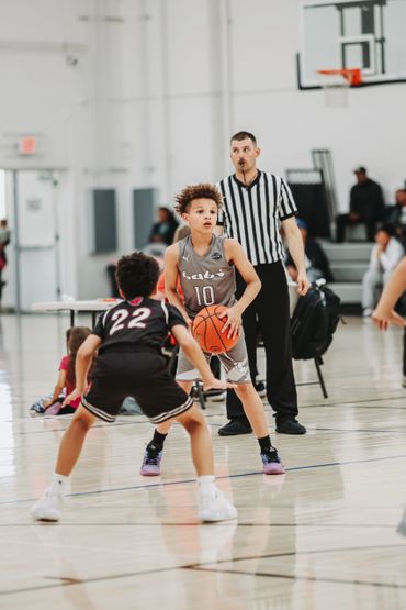 Two young boys playing basketball with a referee watching closely.