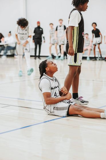 Basketball player sitting on the court showing emotion during a game.