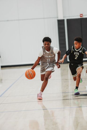 Two young boys playing basketball indoors, one dribbling the ball.