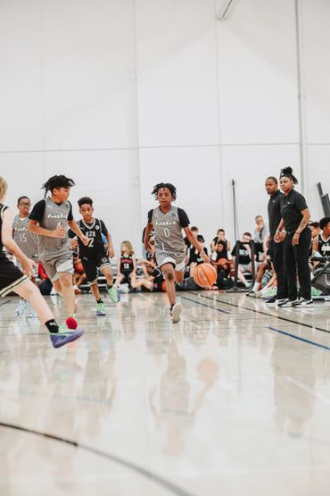 Youth basketball game with players in action on court and coaches watching.