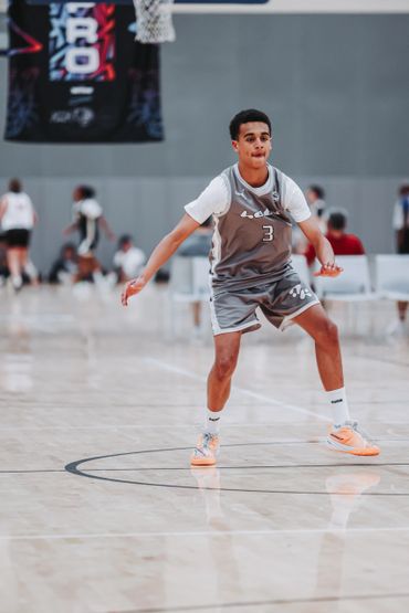 Young basketball player in gray uniform playing defense on court.