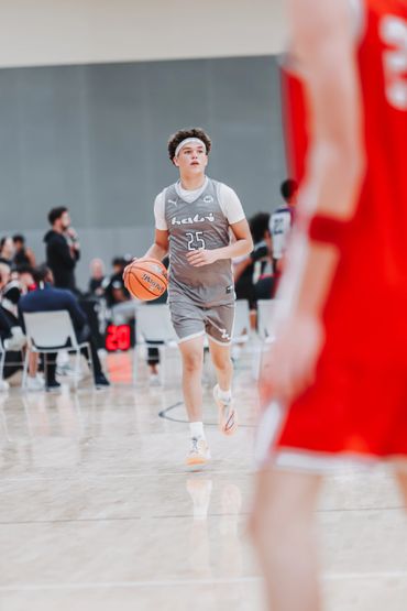 Young basketball player dribbling the ball on court in a gray uniform.
