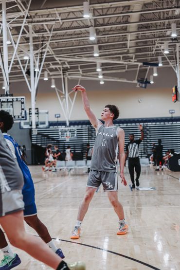 Basketball player in gray uniform takes a shot on an indoor court.