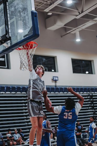 Basketball player in gray jersey scores a layup against defenders in blue jerseys.