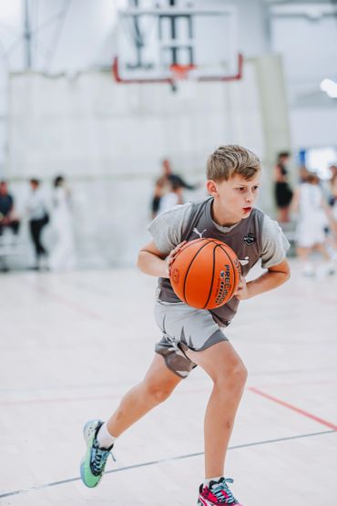 Young boy intensely dribbling a basketball on indoor court.