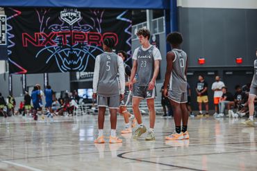 Three basketball players in gray jerseys standing on an indoor court during a game.